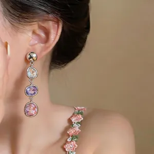 Close-up of tiered crystal drop earrings with pink and purple stones worn by a model.