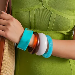 Dettaglio dei bracciali in resina marmorizzata indossati con un abito in maglia verde