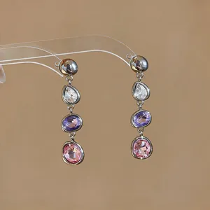 Close-up of elegant dangle earrings featuring clear, purple, and pink teardrop crystals.