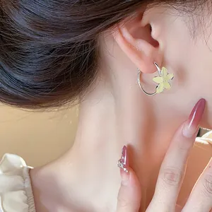 Close-up detail of minimalist silver hoop earrings with a yellow resin flower charm