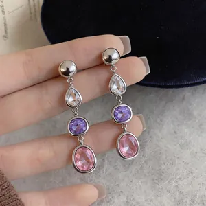 Detailed macro view of geometric teardrop earrings with vibrant pink and purple crystals