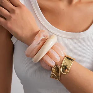 Stacked marble acrylic and gold-tone cuff bracelets on model's wrist