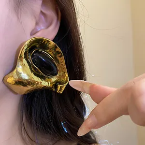 Gros plan d'une grande boucle d'oreille vintage dorée avec résine noire portée.