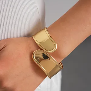 Close-up view of a polished gold-tone geometric cuff bracelet on a woman's wrist.