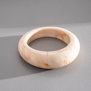 Close-up of a wide acrylic bangle with a polished cream and tan marbled texture detail.