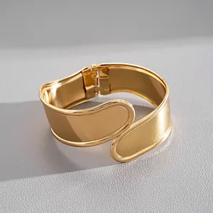 Close-up view of a wide gold-tone geometric bangle with hinge closure and smooth finish.