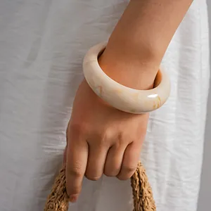 Macro view of a chunky cream marbled acrylic bangle worn on a wrist with a white dress