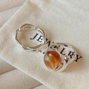Close-up of silver-colored open rings with orange egg-faced stone on jewelry pouch