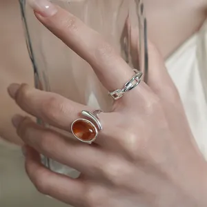 Detail shot of silver chain ring and amber stone ring on hand holding glass