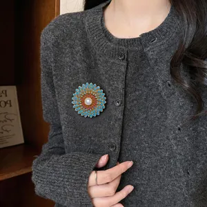 Détail d'une broche fleur avec pétales bleus et perle centrale sur un cardigan gris foncé