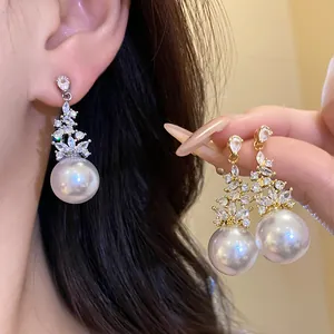 Close-up of elegant zircon flower and large pearl drop earrings in gold and silver finish.