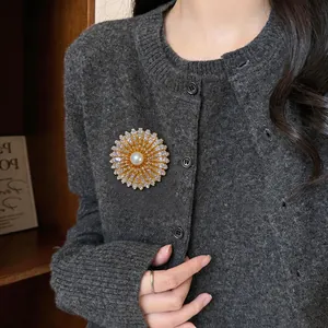 Vue détaillée d'une broche fleur plaquée or 18k avec zircons et perle sur un cardigan.