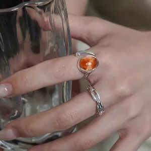 Detail view of a silver ring with an orange marbled stone and a chain-style band.