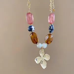 Detalle de cuentas de cerámica mixtas y un colgante de flor dorada en un collar de verano