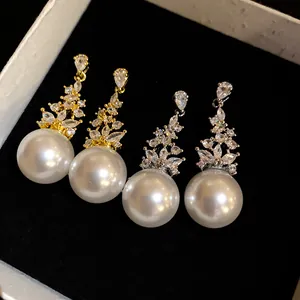Detail view of gold and silver tone earrings with zircons and large pearls