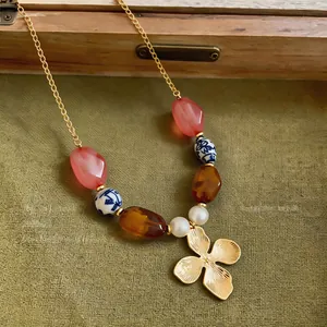 Primer plano de un collar de estilo vacacional con flor de cerámica y perlas sobre tela verde