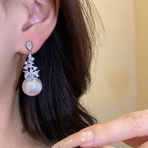 Close-up view of elegant vintage zircon cluster and large pearl dangle earrings worn on ear