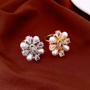 Detailed view of two elegant flower-shaped pearl and zircon rings on a dark brown fabric