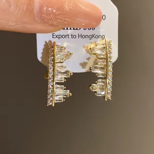 Close-up of irregular geometric earrings featuring clear zircons in a gold-tone setting.