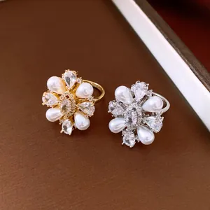 Close-up of elegant flower-shaped pearl and zircon rings in gold and silver finish