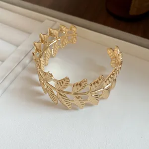 Detailed close-up of elegant gold leaf pattern open cuff bracelet on white textured surface