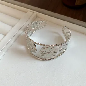 Close-up view of a silver open cuff bracelet with vintage floral and leaf patterns