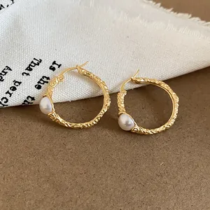 Dettaglio di orecchini vintage dorati con texture stropicciata e accenti di perle