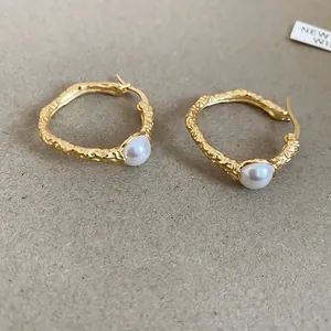 Dettaglio di orecchini a cerchio vintage dorati plissettati con perla bianca fine