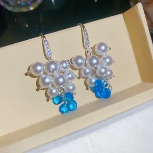 Dettaglio di orecchini a perla a forma di uva con zirconi e perline blu traslucide.
