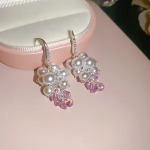 Dettaglio di orecchini a grappolo con perle bianche e cristalli rosa su scatola per gioielli.