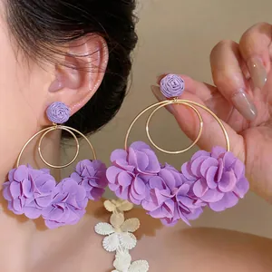 Dettaglio di orecchini a fiore in chiffon viola con perni a rosa in rafia stile vacanza.