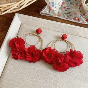 Dettaglio macro degli eleganti orecchini a fiore in chiffon rosso con cerchi dorati