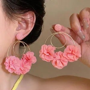 Dettaglio di orecchini a cerchio con fiori in chiffon rosa e bottone in rafia elegante