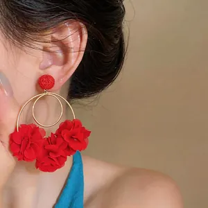 Dettaglio di orecchini a fiore in chiffon rosso con rafia e cerchi d'oro all'orecchio.
