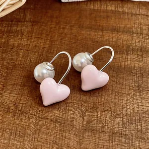 Close-up of sweet pink heart earrings with white pearl detail on wooden background.