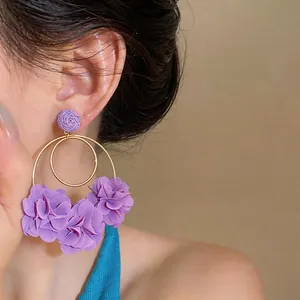 Primo piano di orecchini a cerchio con fiori in chiffon viola e rafia su una modella