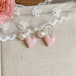 Detail of pink heart-shaped earrings with pearl accents and silver hook on lace background