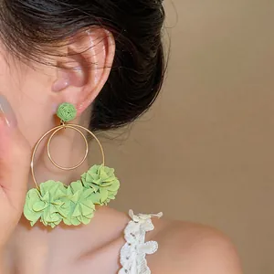 Dettaglio di orecchini a fiore in raffia verde con doppi cerchi dorati su una modella