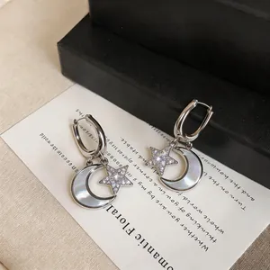 Gros plan détaillé de boucles d'oreilles créoles avec lune en nacre et étoiles en zircon brillant