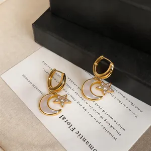 Gros plan sur d'élégantes boucles d'oreilles étoile et lune dorées avec nacre et zircon