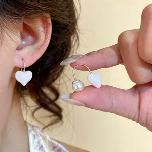 Close-up of elegant S925 silver enamel heart earrings with pearl accent on model.