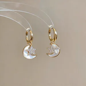 Gros plan de boucles d'oreilles étoile et lune dorées avec zircon et nacre incrustés