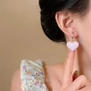 Close-up view of a sweet pink heart drop earring worn by a model, silver hoop