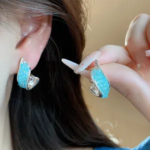 Close-up detail showing the brilliant blue crushed glass inlay on twisted silver earrings