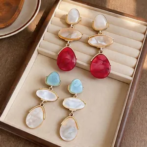 Elegant resin droplet earrings with colorful geometric shapes displayed on a beige velvet tray