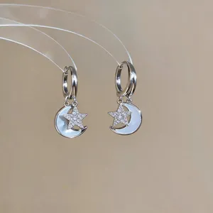 Détail de boucles d'oreilles créoles lune et étoile en zircon et nacre.