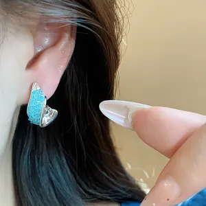 Close-up of elegant blue irregular glass stud earring with silver needle worn on ear.