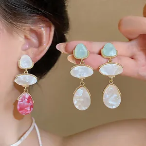 Detailed view of vibrant resin oval teardrop earrings worn by model and held by hand