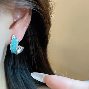 Detailed view of irregular silver stud earrings featuring textured blue glass inserts