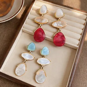 Close-up of elegant resin teardrop earrings in red and blue shades on a soft beige jewelry tray.